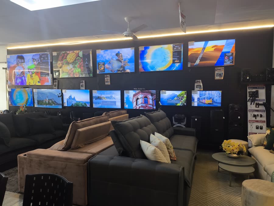 Parede de Smart TVs ligadas sobre a área de sofás e estofados do Grupo JNF
